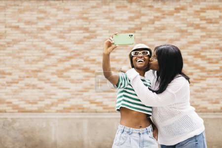 Retrato de dos jóvenes mujeres negras alegres besándose y tomando una vida selecta en un entorno al aire libre.