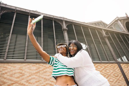 Retrato de dos jóvenes mujeres negras alegres abrazando y tomando una vida selecta en un entorno al aire libre.