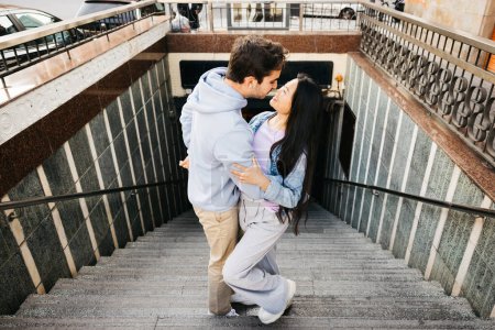 Interracial cheerful couple on a date, getting off the subway in a city. Young man and woman kissing on subway stairs.
