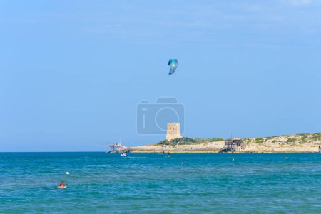 Photo for Vieste, Italy. Kitesurfer near the Scialmarino beach. The trabucco of Tufara Bay and the Porticello Tower on the background. Summer day along the coast of Vieste. September 7, 2022 - Royalty Free Image