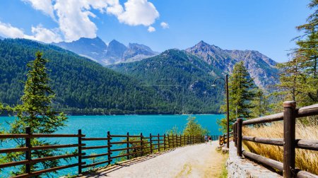 Photo for Ceresole Reale, Italy. View of Lake Ceresole on a sunny summer day. A family walks along the path. Alps mountains in the background. - Royalty Free Image