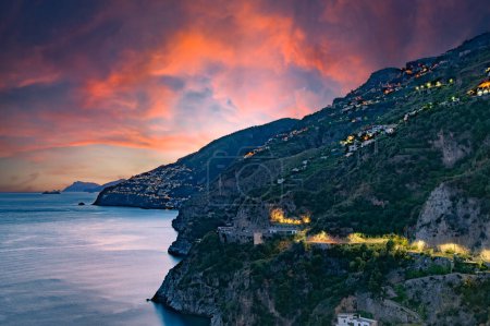Amalfiküste, Italien. Blick über Praiano an der Amalfiküste bei Sonnenuntergang. Straßen- und Hausbeleuchtung in der Abenddämmerung. In der Ferne am Horizont die Insel Capri. Amalfiküste. Meereslandschaft.