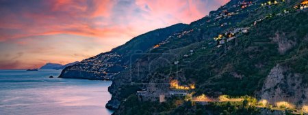 Amalfiküste, Italien. Blick über Praiano an der Amalfiküste bei Sonnenuntergang. Straßen- und Hausbeleuchtung in der Abenddämmerung. In der Ferne am Horizont die Insel Capri. Meereslandschaft. Kopfbild mit Banner.