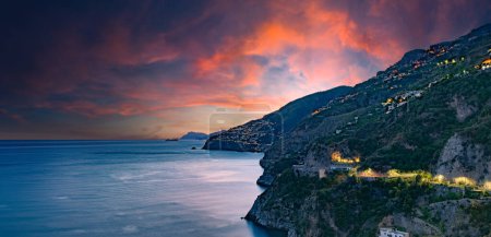 Amalfiküste, Italien. Blick über Praiano an der Amalfiküste bei Sonnenuntergang. Straßen- und Hausbeleuchtung in der Abenddämmerung. In der Ferne am Horizont die Insel Capri. Amalfiküste. Kopfbild mit Banner.