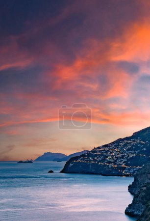 Côte amalfitaine, Italie. Vue sur Praiano sur la côte amalfitaine au coucher du soleil. Lumières de rue et de maison au crépuscule. Au loin l'île de Capri à l'horizon. Paysage marin. Image verticale.