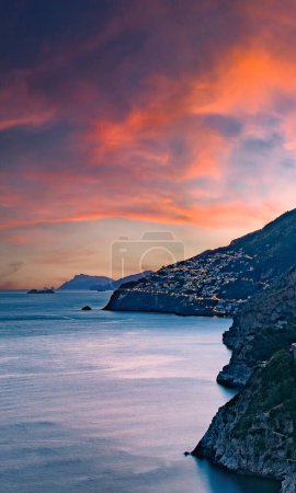 Côte amalfitaine, Italie. Vue sur Praiano sur la côte amalfitaine au coucher du soleil. Lumières de rue et de maison au crépuscule. Au loin l'île de Capri à l'horizon. Paysage marin. Image verticale.