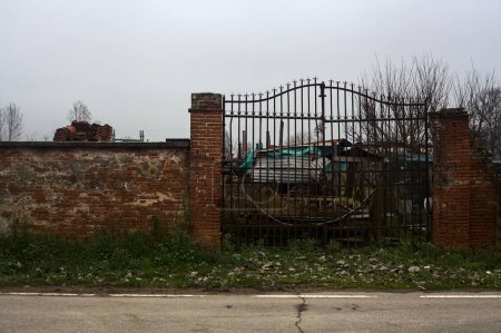 Photo for Gate in a brick boundary wall at the edge of a road with building equipments behind the grating in the italian countryside - Royalty Free Image