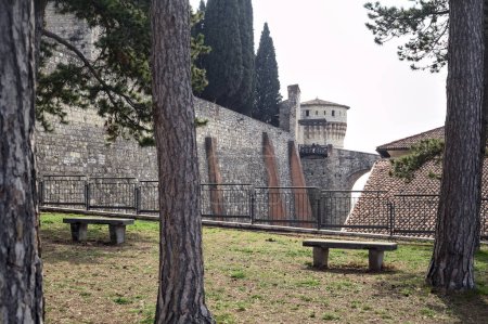 Photo pour Terrasse avec des arbres et des bancs à côté d'un mur frontière d'un château avec un pont au loin - image libre de droit