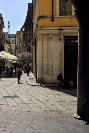 Foto de Calle estrecha a la sombra con tiendas y gente que pasa en un día soleado en una ciudad italiana - Imagen libre de derechos