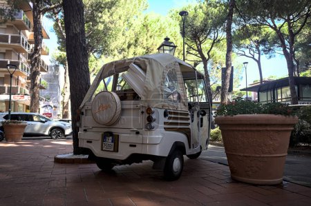 Photo for White Piaggio Ape Calessino on the pavement next to shop windows in an italian town by the seaside - Royalty Free Image