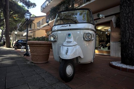 Photo for White Piaggio Ape Calessino on the pavement next to shop windows in an italian town by the seaside - Royalty Free Image