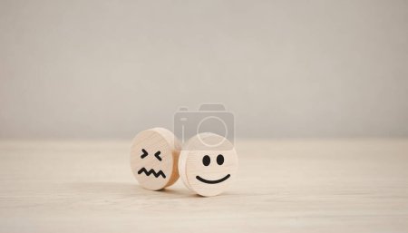 glückliche Emotion Gesicht auf Holzstück mit unglücklichem hinter für Zufriedenheitsumfrage, Beurteilung der psychischen Gesundheit