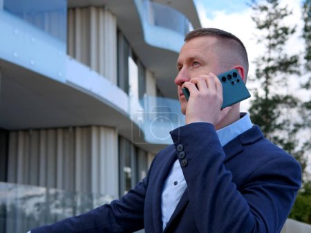 Ein Geschäftsmann führt ein Telefongespräch vor einem Bürogebäude, gekleidet in formelle Geschäftskleidung. Das professionelle Auftreten des Geschäftsmannes wird offensichtlich, wenn er wichtige Angelegenheiten diskutiert.