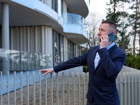 Ein Geschäftsmann führt ein Telefongespräch vor einem Bürogebäude, gekleidet in formelle Geschäftskleidung. Das professionelle Auftreten des Geschäftsmannes wird offensichtlich, wenn er wichtige Angelegenheiten diskutiert.