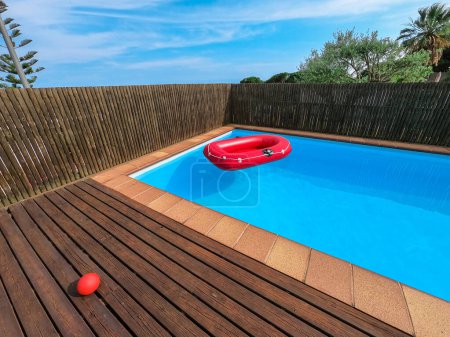Photo for Red inflatable boat floating in a private swimming pool in a house backyard. Summer, recreation, holidays, vacation concept. No people. Horizontal - Royalty Free Image