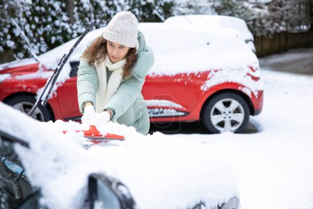 Foto de Young woman cleaning her car from snow in backyar - Imagen libre de derechos
