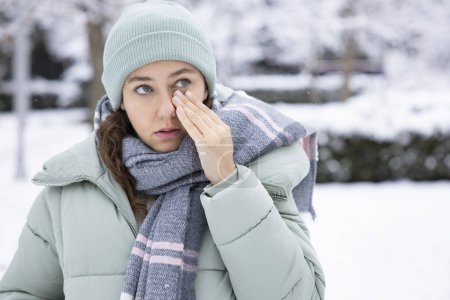 Foto de Mujer joven que tiene picazón en los ojos problema de salud. Mujer enferma en invierno nieve tocando su ojo sensible - Imagen libre de derechos