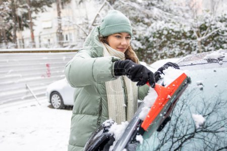 Photo for Young woman cleaning her car from snow in backyar - Royalty Free Image