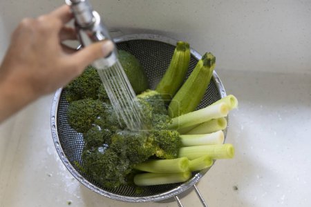 Téléchargez les photos : Woman hand washing vegetables on kitchen counter. Zucchini, leek and broccoli - en image libre de droit