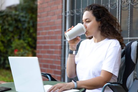 Téléchargez les photos : Young woman sitting on a chair in backyard garden and looking at lapto - en image libre de droit