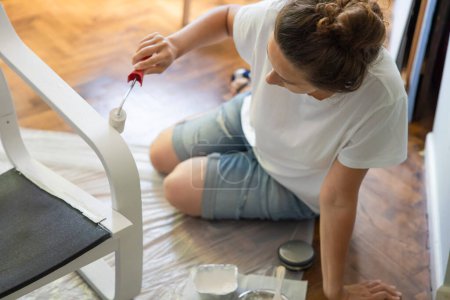 Téléchargez les photos : Young woman painting a black wooden chair in white. DIY project concept - en image libre de droit