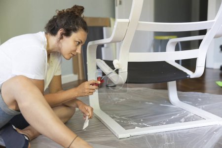 Foto de Mujer joven pintando una silla de madera negra en blanco. Concepto de proyecto DIY - Imagen libre de derechos