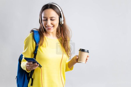 Téléchargez les photos : High school student attractive young woman with headphones and backpack at gray background - en image libre de droit