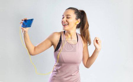 Téléchargez les photos : Sporty young woman in earphone holding smartphone and dancing over gray backgroun - en image libre de droit