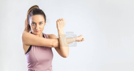 Téléchargez les photos : Déterminé jeune femme sportive étirant le bras avant l'entraînement sur fond gris - en image libre de droit