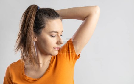 Photo for Young woman smelling her underarms in studio gray backgroun - Royalty Free Image