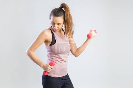 Téléchargez les photos : Young sporty woman exercising with dumbbells over gray background - en image libre de droit