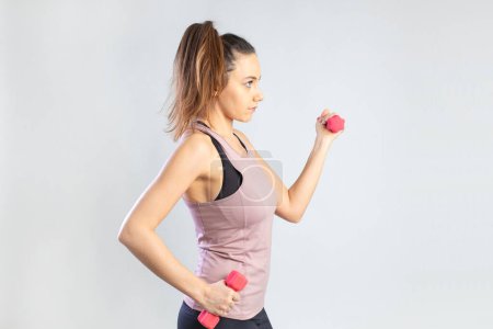 Photo for Young sporty woman exercising with dumbbells over gray background - Royalty Free Image