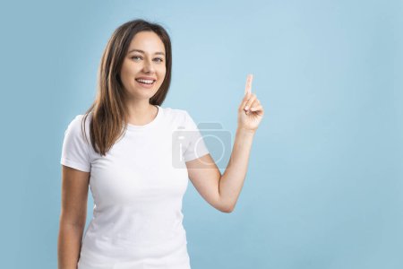 Photo for Young excited happy brunette woman pointing away and smile isolated on blue background - Royalty Free Image