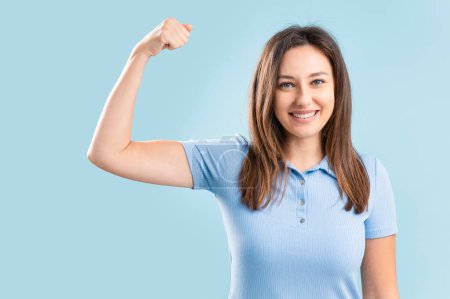 Foto de Self proud cheerful young woman shows her biceps on blue background. Women in business, women's power concepts - Imagen libre de derechos