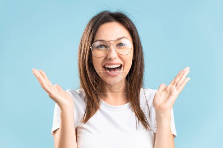 Foto de Attractive cheerful woman with eyeglasses showing wow gesture isolated over blue background - Imagen libre de derechos