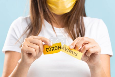 Photo for End of a coronavirus quarantine concept. Young female in face mask tearing the paper with the word Coronavirus. Pandemic of COVID-19 is over - Royalty Free Image