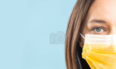 Photo for Young woman wearing medical face mask on blue background. Protection against Covid-19, prevention the spread of the viru - Royalty Free Image