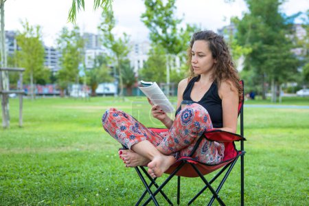 Foto de Young woman sitting on camping chair and reading a book - Imagen libre de derechos