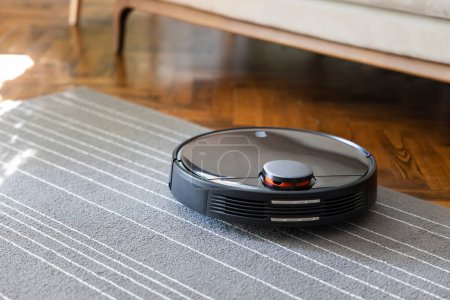 Téléchargez les photos : Aspirateur robot sur le tapis. Nettoyage dans le salon à la maison - en image libre de droit