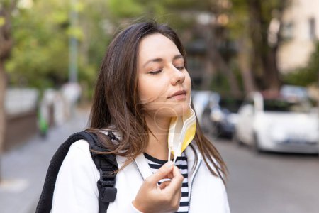 Foto de Mujer joven que alivia quitarse la máscara para respirar aire fresco en la calle - Imagen libre de derechos