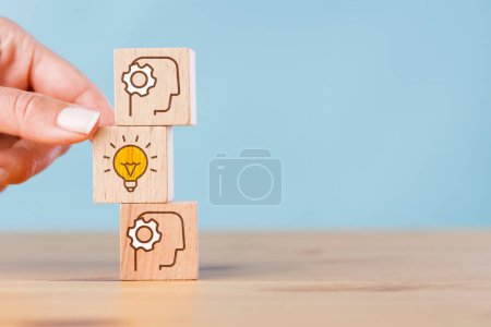 Photo for Woman hand picking light bulb icon out of wooden cubes with human head symbol - Royalty Free Image