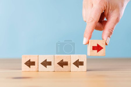 Photo for Woman hand holding block with red arrow facing the opposite direction other arrows. Think different, standing out from the crowd - Royalty Free Image