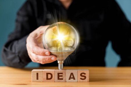 Photo for Man holding a glowing light bulb on ideas wording on wooden block for creative idea. Thinking and innovation concept. - Royalty Free Image