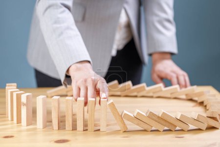 Photo for Businesswoman stopping wooden block from falling in the line of domino with risk concept - Royalty Free Image