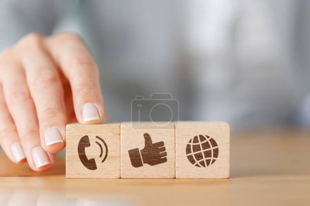 Foto de Businesswoman mano elegir bloque de madera icono de símbolo de cubo teléfono, pulgares hacia arriba y el mundo. Página web contáctenos o redes sociales, concepto de comunicación global - Imagen libre de derechos