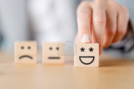 Foto de Mano del cliente elegir cara sonriente en cubo de madera, calificación de servicio, concepto de satisfacción - Imagen libre de derechos