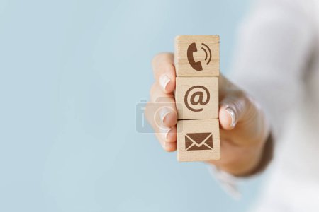 Foto de Mano femenina sosteniendo un cubo de madera símbolo de teléfono, sobre de correo electrónico y signo de dirección. Página web contáctenos o redes sociales concep - Imagen libre de derechos
