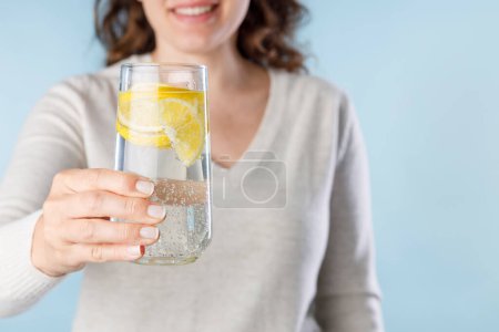 Foto de Mujer joven sosteniendo un vaso de agua mineral con limón. Estilo de vida saludable, dieta y forma física - Imagen libre de derechos