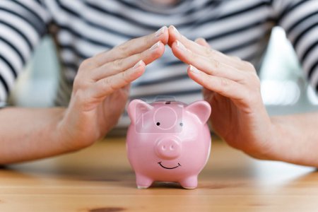 Photo for Woman hands covering the pink cute piggy bank. Protect your savings - Royalty Free Image