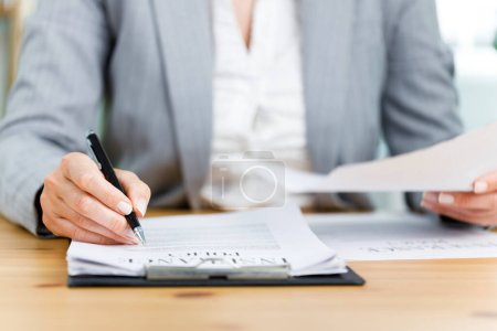 Photo for Close-up shot of businesswoman filling out insurance policy in her office - Royalty Free Image